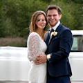 Et smilende brudepar, Thea og Marius, står foran en elegant pyntet hvit bil på bryllupsdagen sin.
